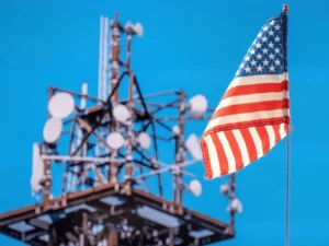 American flag near telecommunications tower, blue sky.