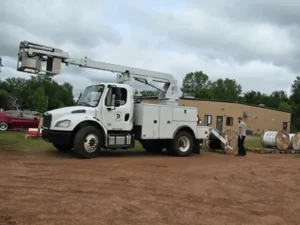 Utility truck with elevated boom arm outside.