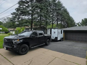 Black truck towing trailer in suburban driveway.
